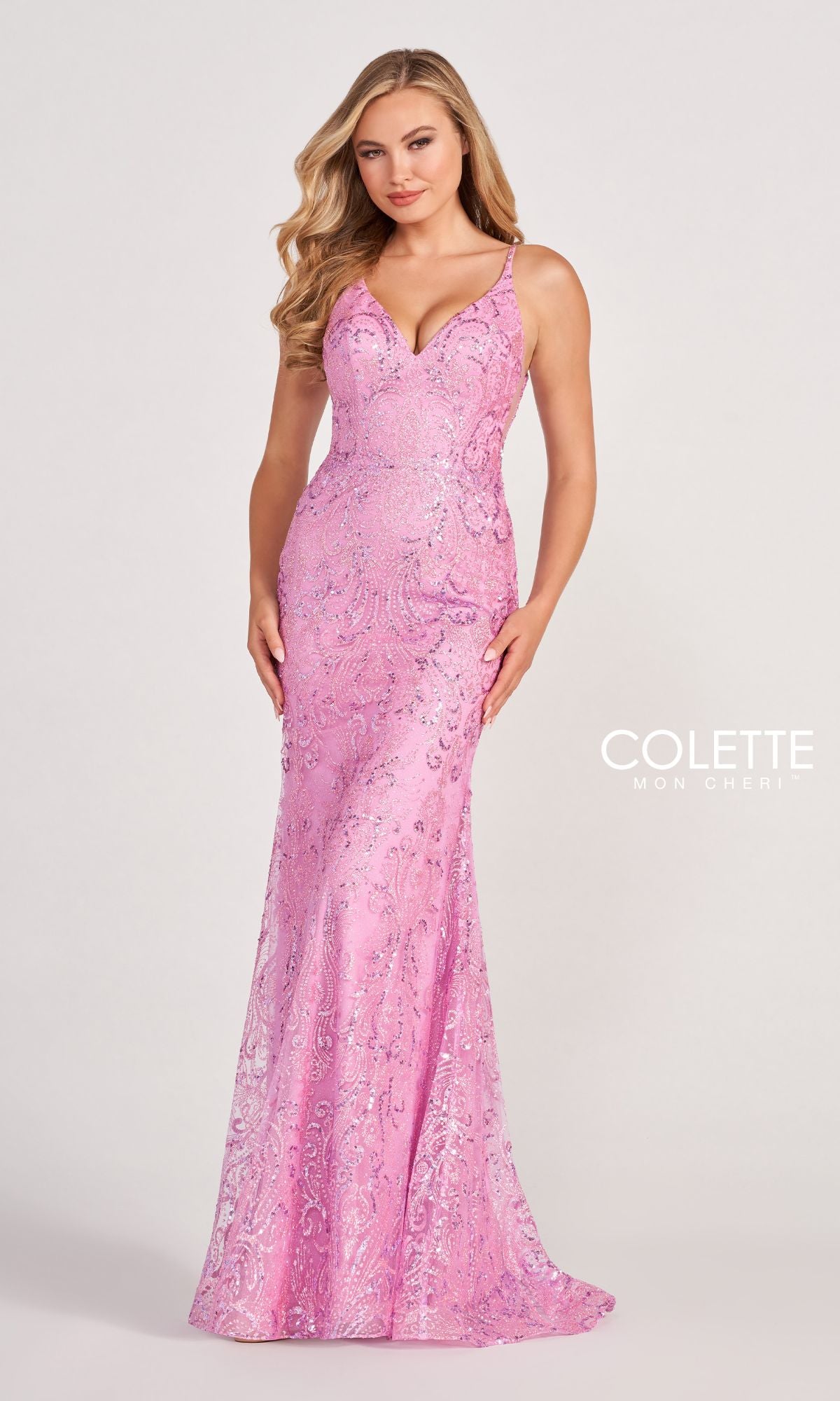 A woman wears the Colette CL2019 Long Prom Dress in Glitter-Sequin, a fitted, sleeveless, floor-length pink gown with a V-neckline and intricate sparkling patterns, standing against a plain light background.